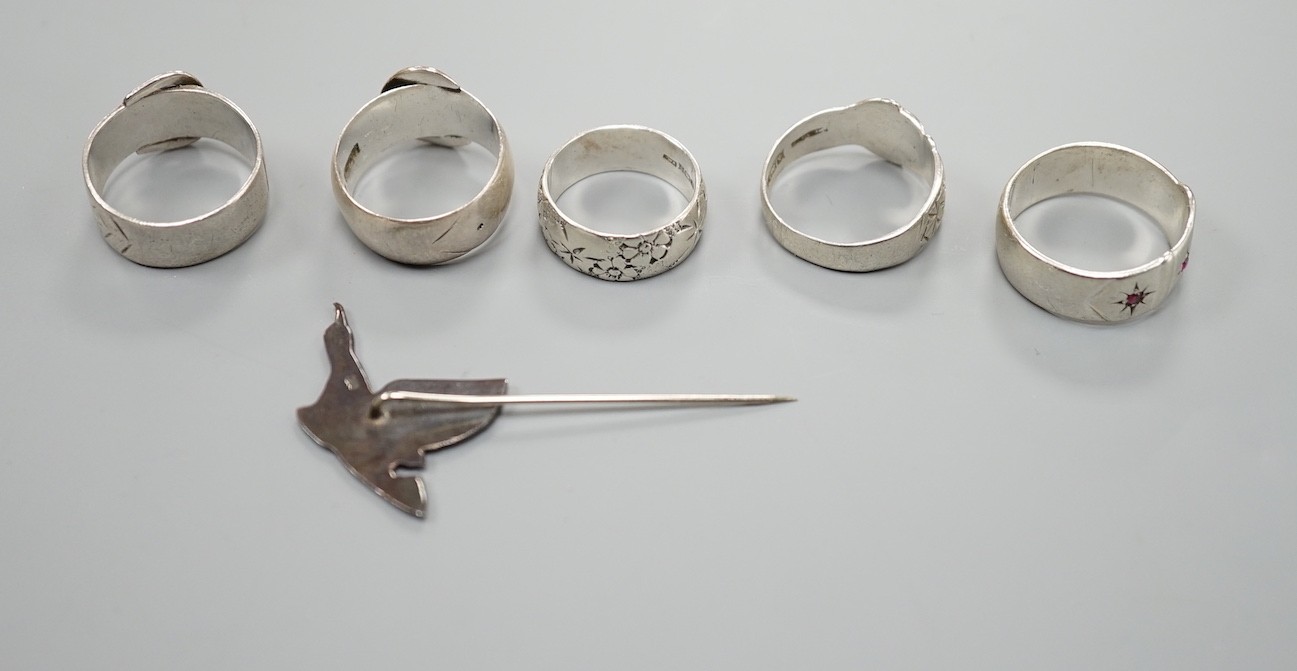 Four assorted silver buckle rings, including one set with red stones, an engraved silver band and a 925 duck stick pin.